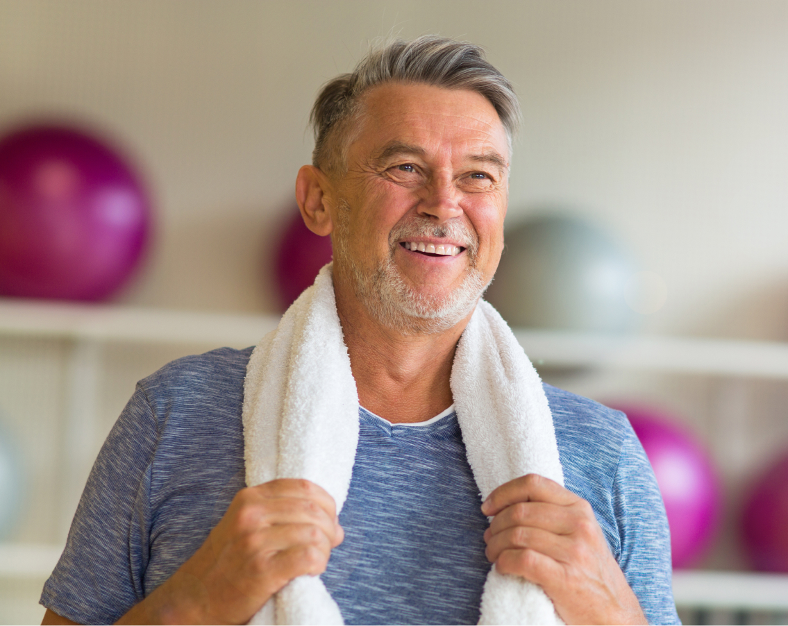 Middle aged teacher in a standing with a towel around his neck after pilates class