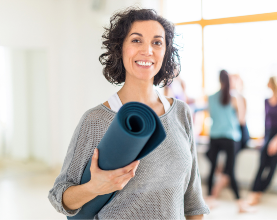 Middle Aged Female Teacher At A Yoga Class, Holding Her Mat, About To Go In For A Discounted Class.