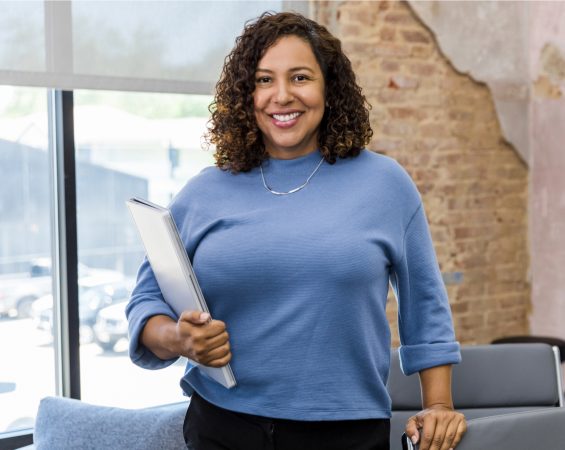 Teacher Standing In Teacher's Lounge Window, Holding A Laptop She Got A Discount On Under Her Arm.